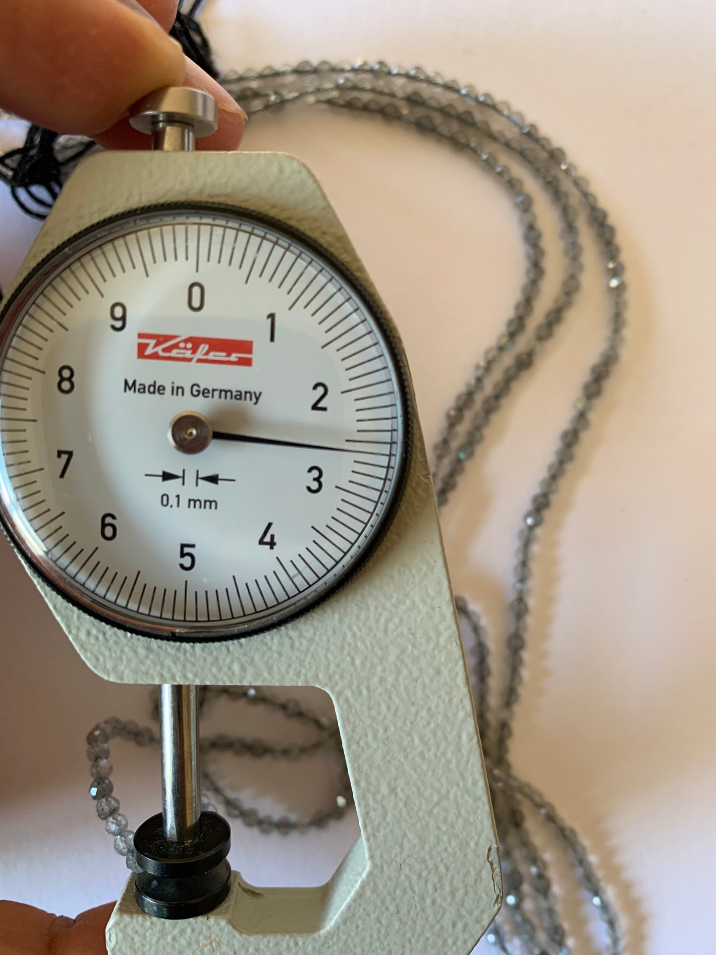 A dial gauge measures the Labradorite Faceted Rondelle 2.5-2.7mm gemstone.