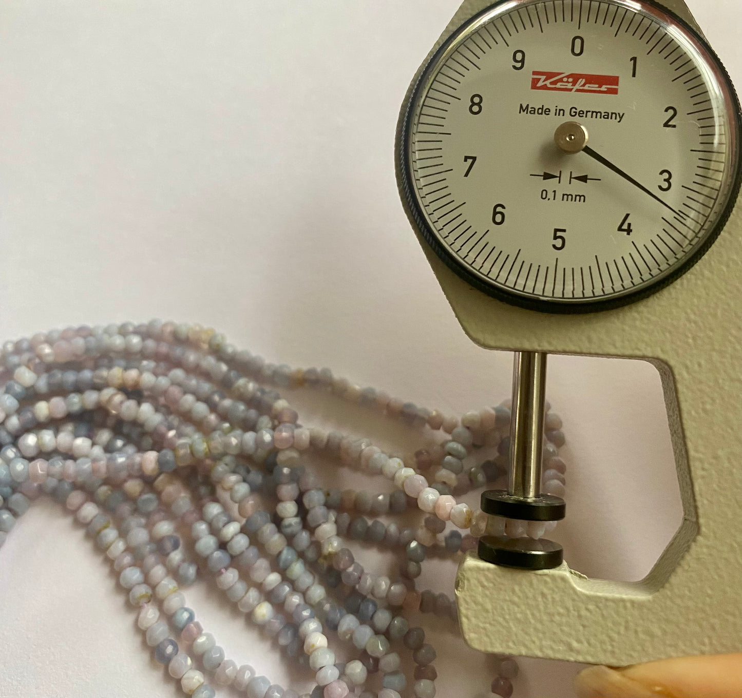 Close-up of a measuring dial gauge beside colourful Lavender Opal beads.