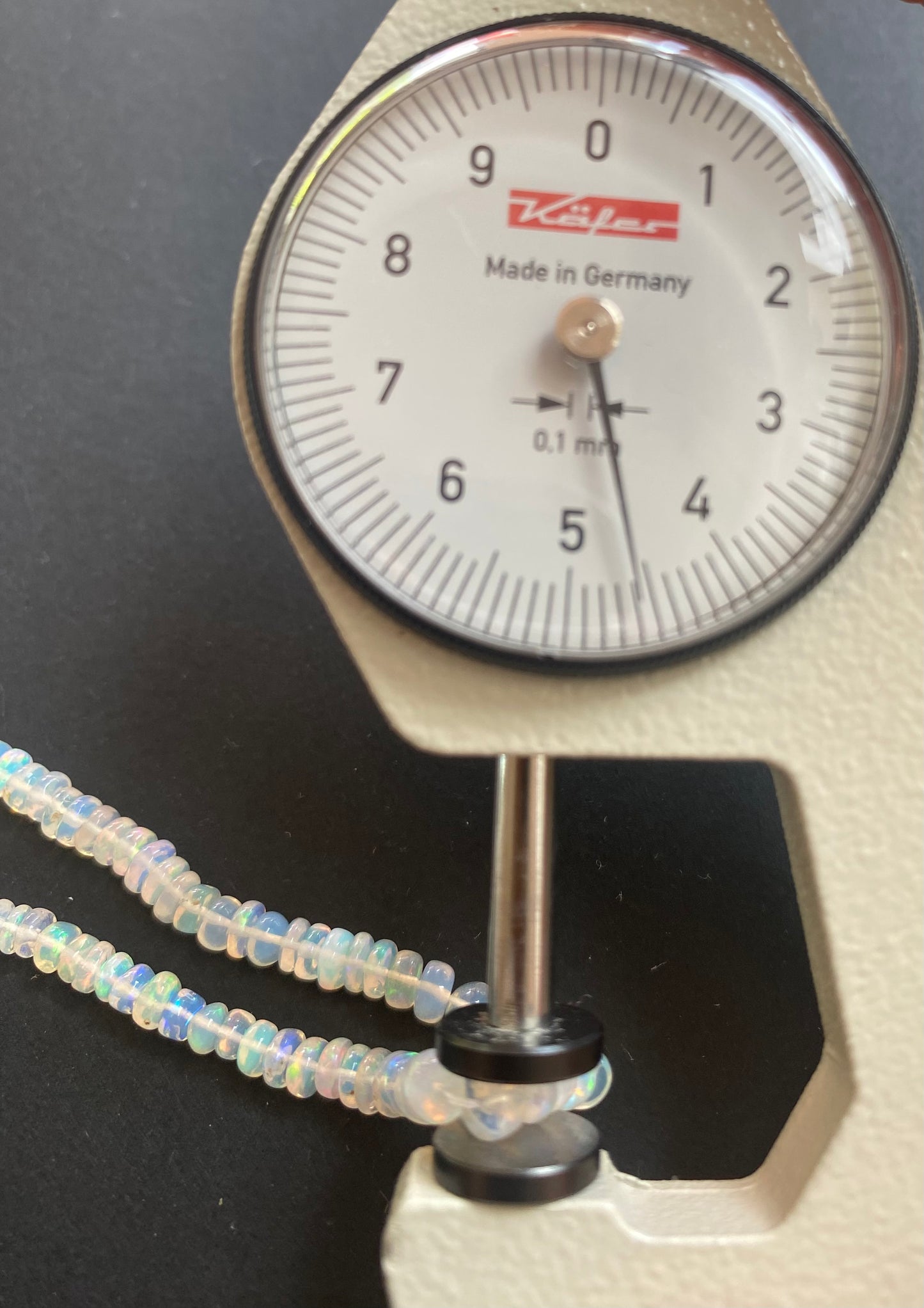 A person uses a dial gauge to measure a Opal Smooth Rondelle, sized 3.3-4.5mm.