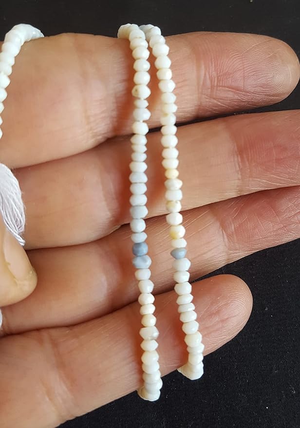 A hand holding a strand of white denim opal beads, featuring a faceted rondelle design that catches the light.
