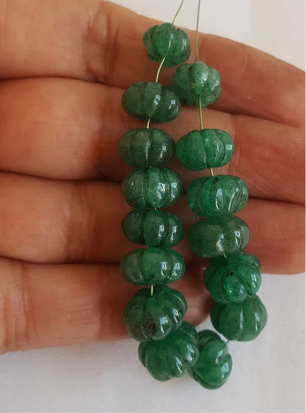 A person holding a carved rondelle emerald gemstone strand, showcasing its green facets and elegant design.