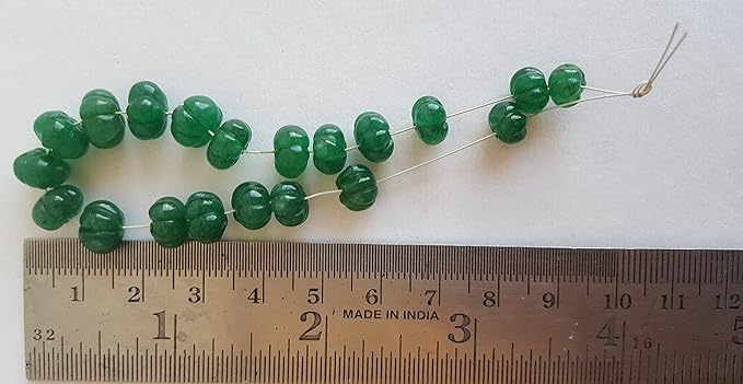 Close-up of a measuring ruler alongside green Emerald beads, showcasing their carved rondelle shape and size.