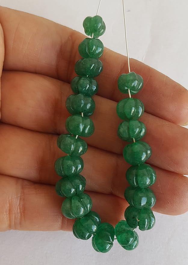 A strand of green emerald beads, featuring carved rondelle shapes, showcasing their vibrant colour and shine.