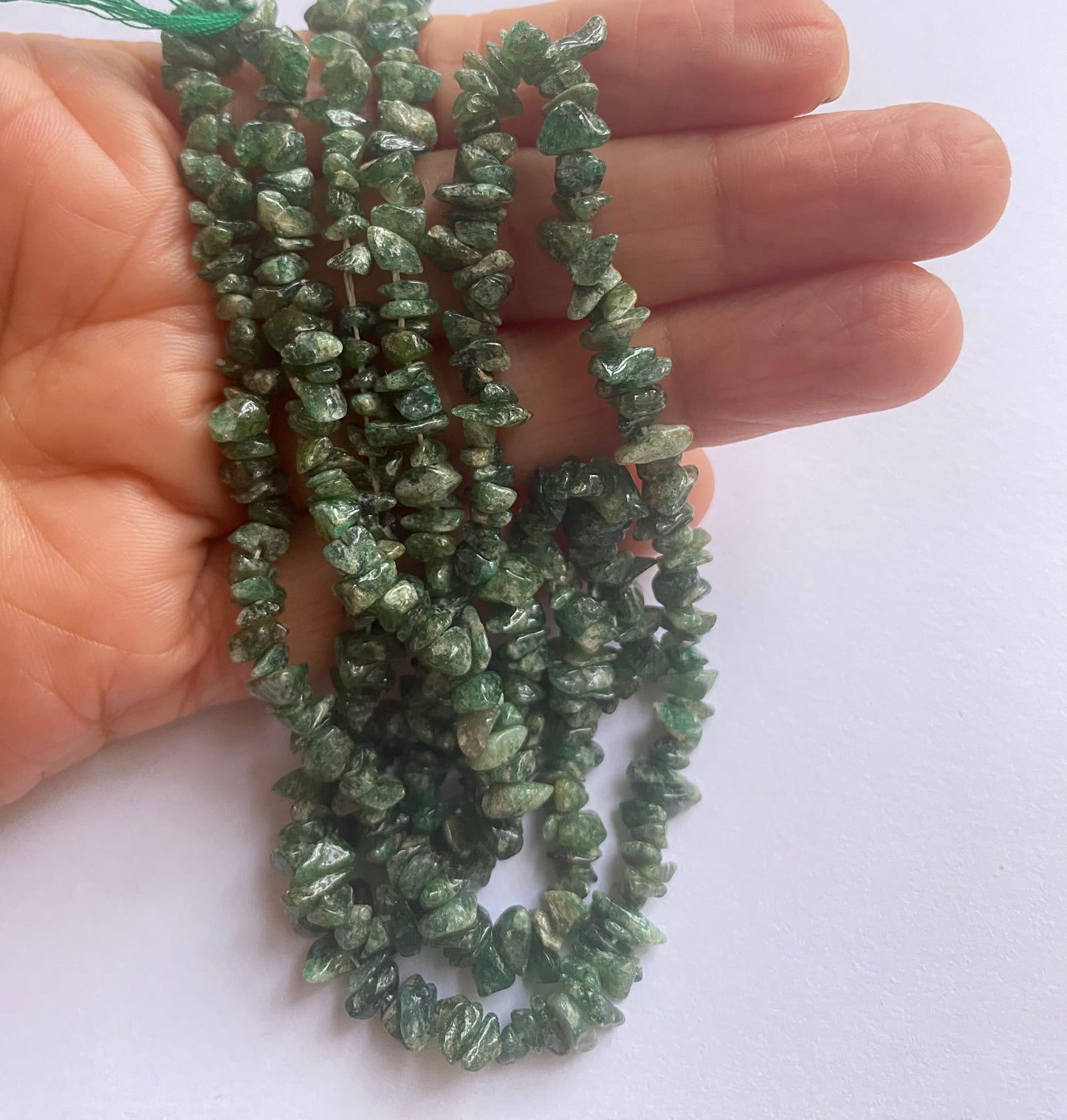 A person holding a emerald chip gemstone strand, showcasing its facets and elegant design.