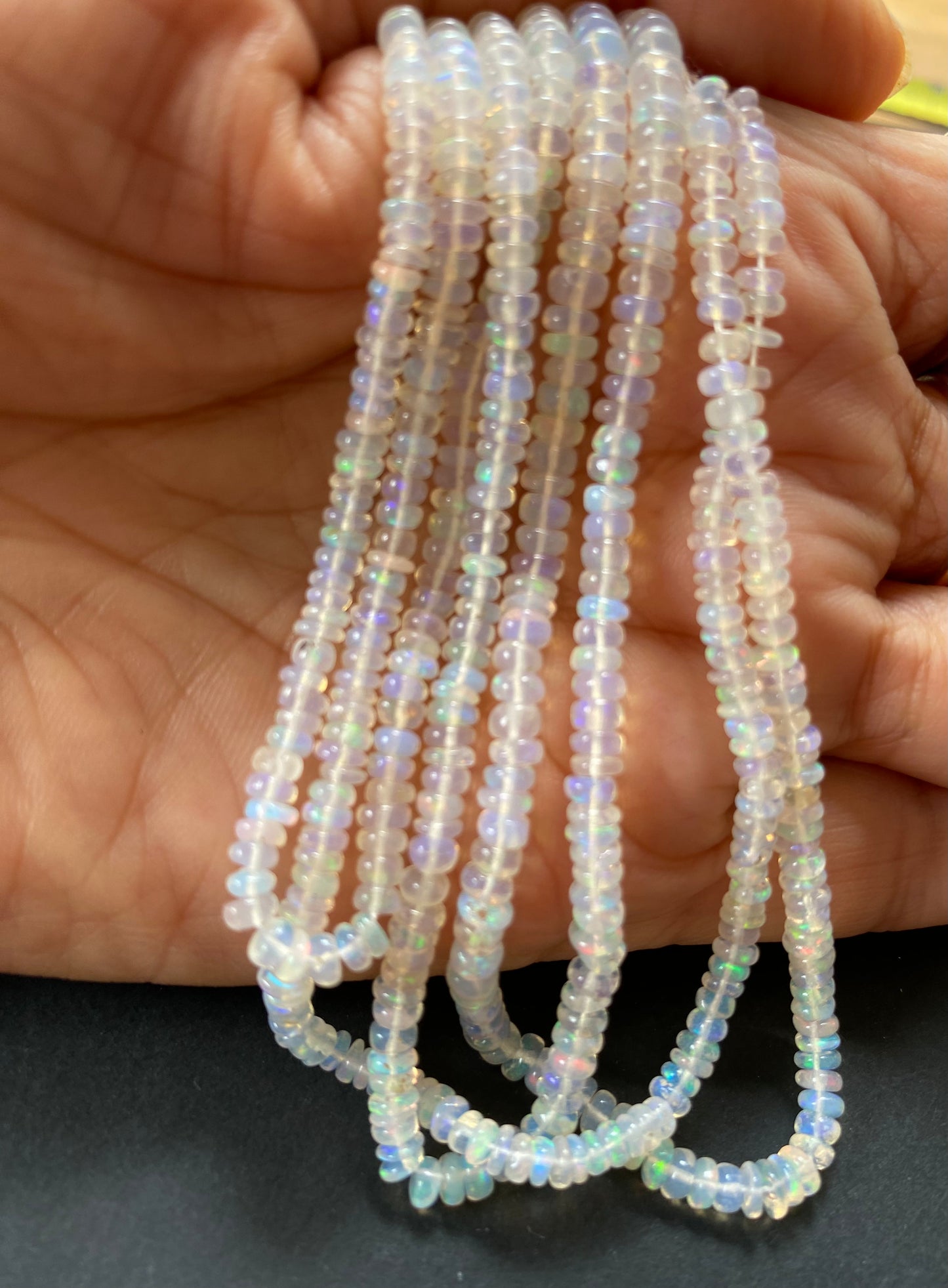 Close-up of a person grasping a strand of smooth white ethiopian Opal beads, each 3.2-4.2mm in size, highlighting their beauty.