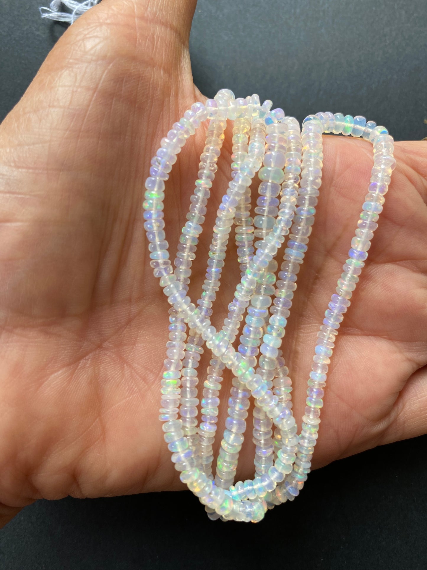 A person holding a smooth strand of ethiopian Opal beads, measuring 3.2-4.2mm, showcasing their elegant white colour.