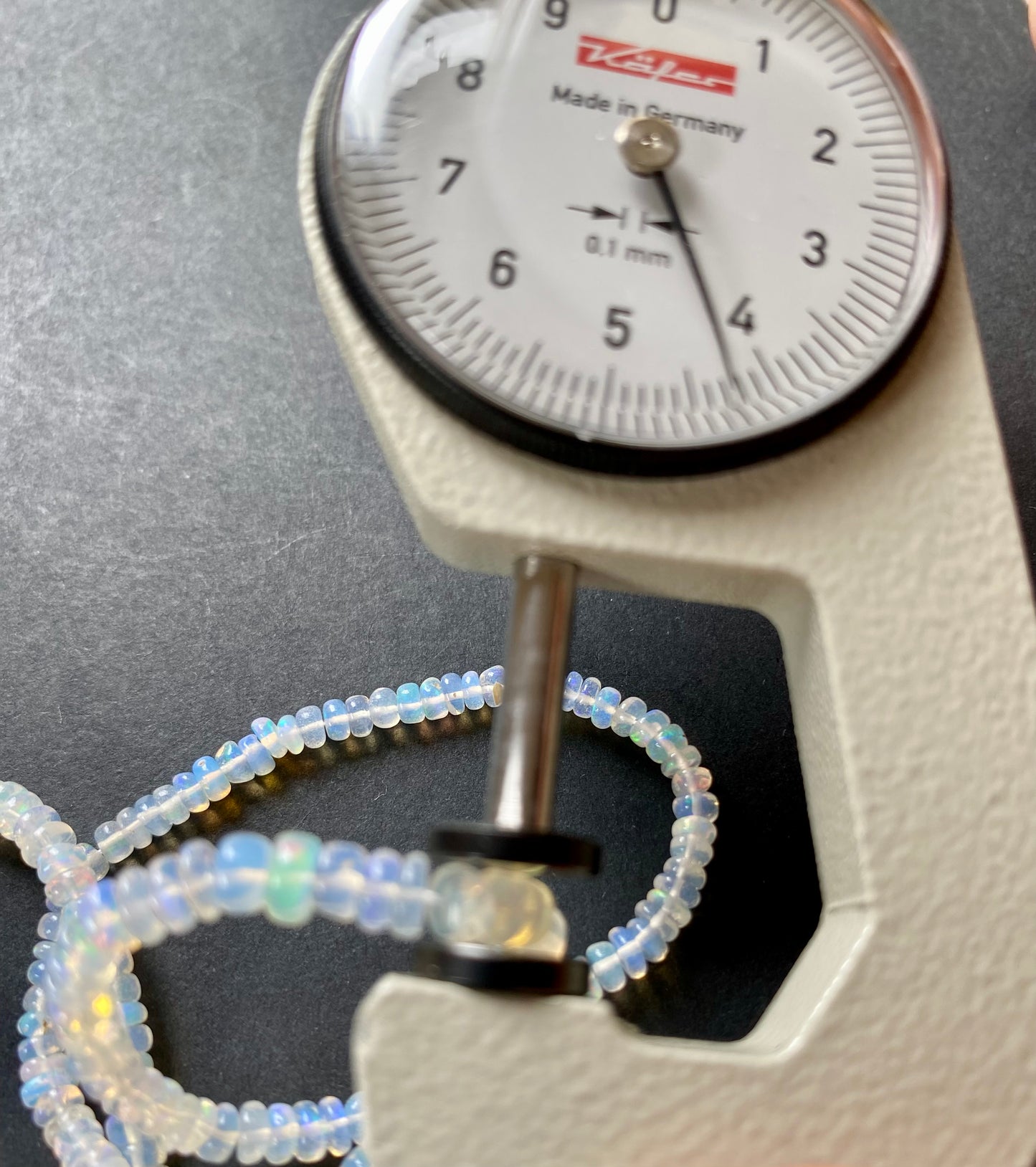 Close-up of a measuring dial gauge tool alongside a string, highlighting the precision of measurements for ethiopian Opal jewellery.