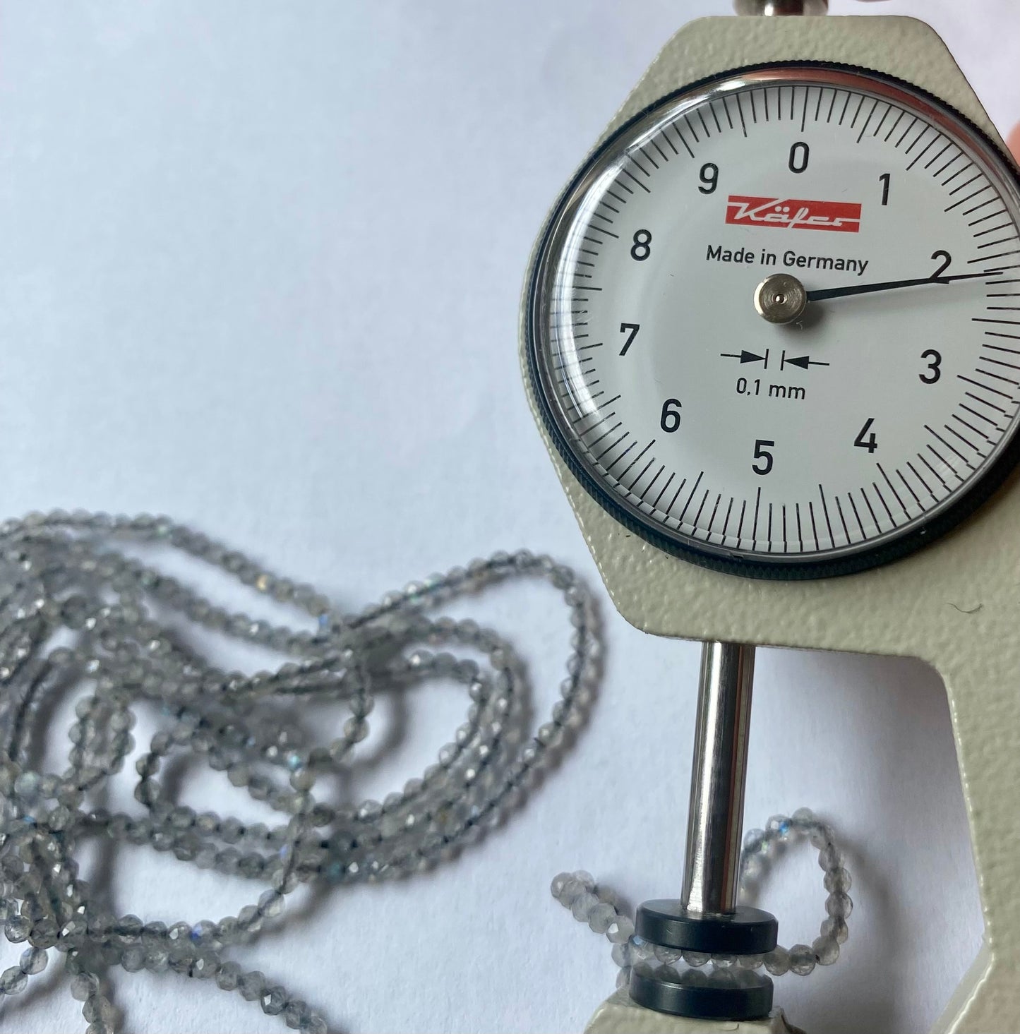 A dial gauge measures the Labradorite faceted rondelle 2.2mm gemstone, ensuring precise sizing.