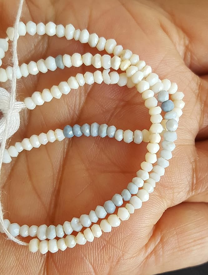 A person holding a strand of faceted rondelle denim opal gemstone beads, showcasing their shimmering white surface