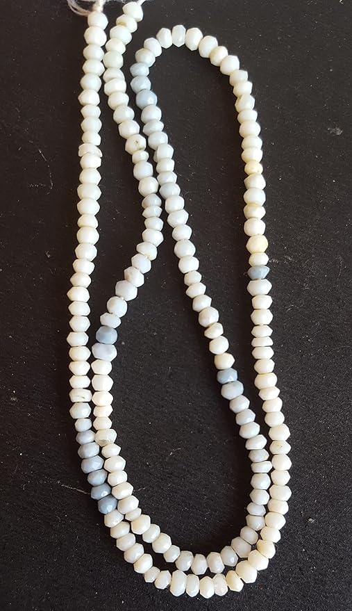 White and blue faceted rondelle denim opal beads arranged on a sleek black surface, showcasing the vibrant colours of these semi-precious gemstones.