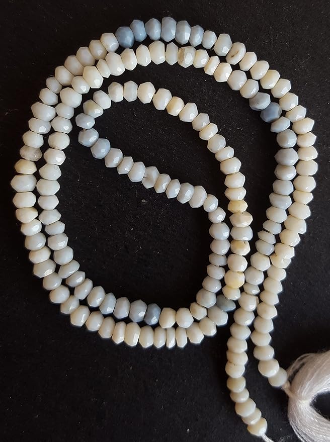 A close-up of a strand of white and blue faceted rondelle denim opal semi-precious gemstone beads resting on a smooth black surface