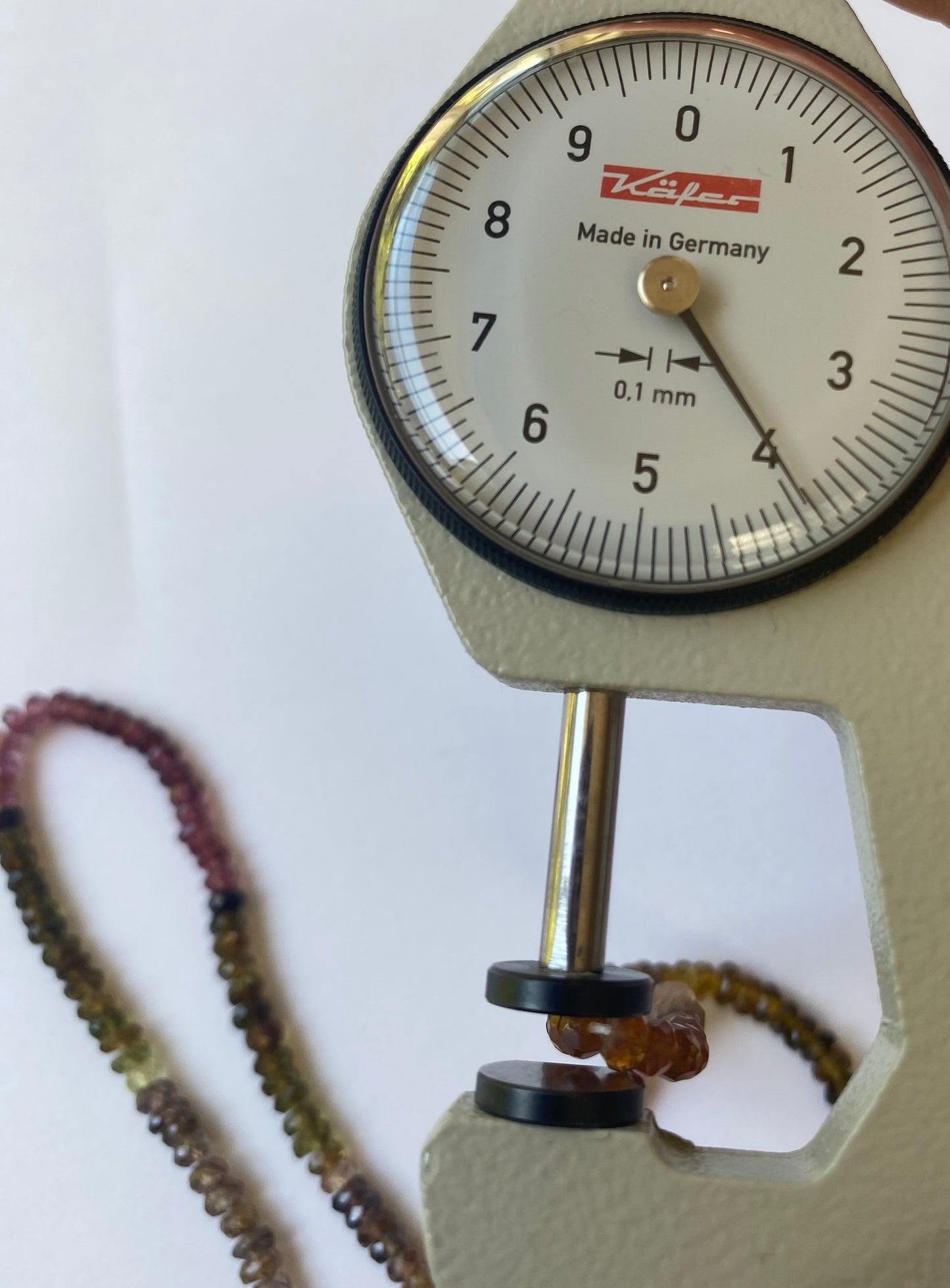 Close-up image of a dial gauge with a red string, emphasising the 3.5-4mm faceted tourmaline beads.