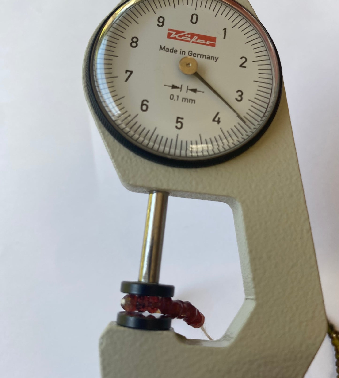 Close-up of a dial gauge featuring a red string, showcasing faceted tourmaline beads sized 3.5-4mm.