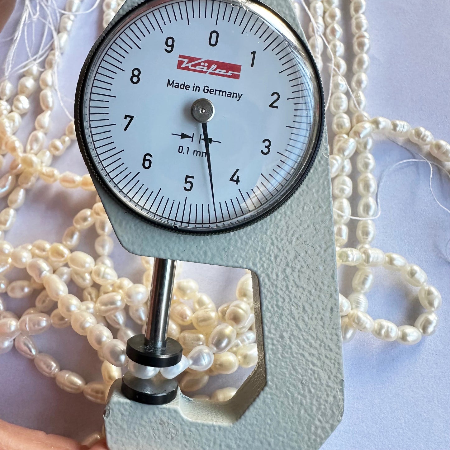 A dial gauge measures the Fresh Water Pearl smooth fancy shape 4mm to 4.5mm gemstone, ensuring size accuracy.