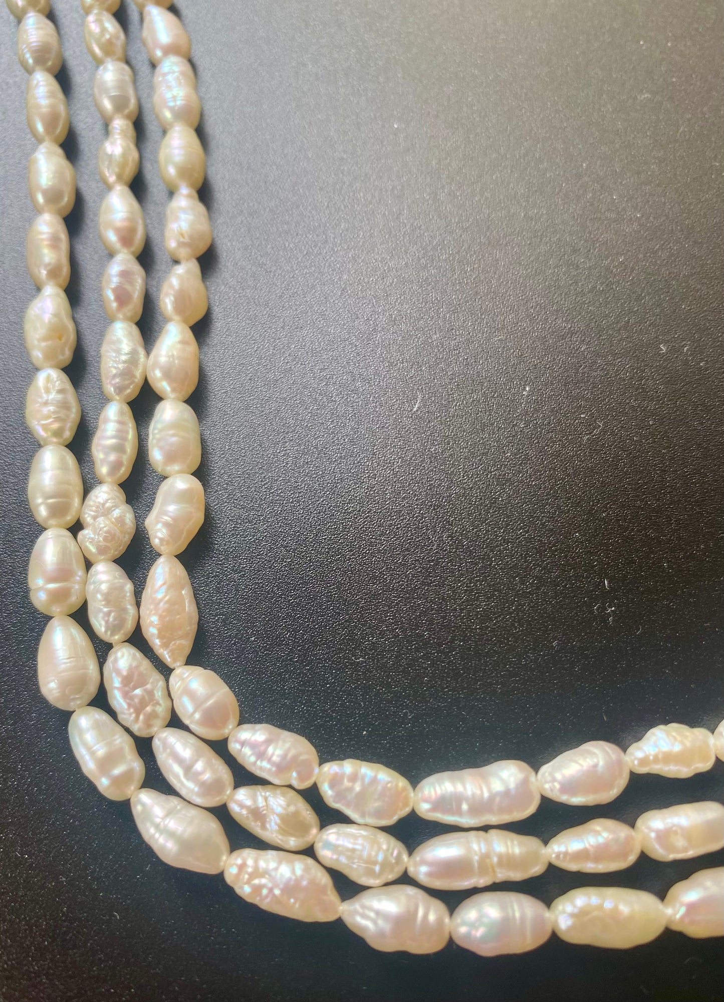 Beautiful strands of freshwater baroque rice pearl beads resting on a sleek black background, showcasing their lustre.