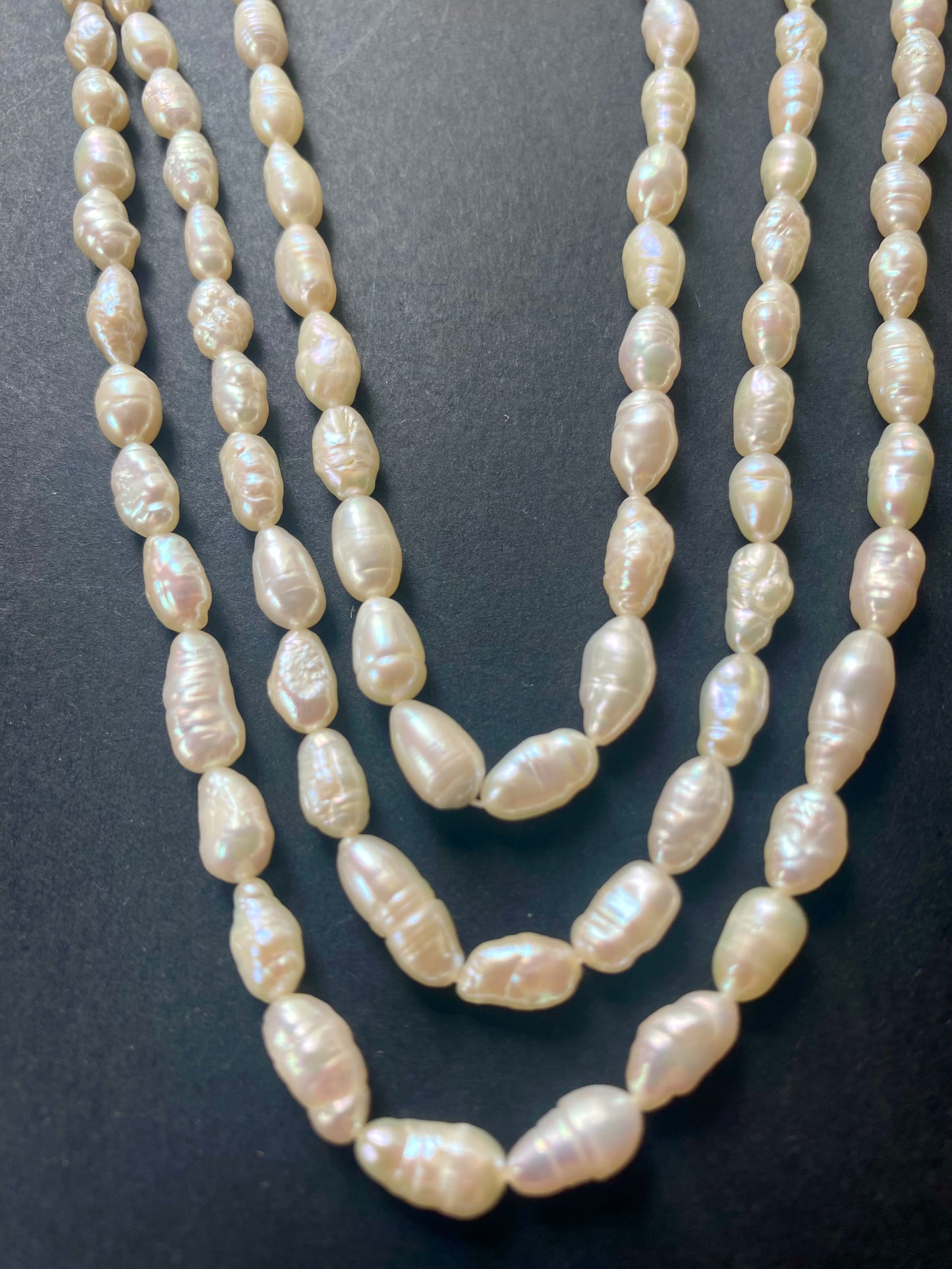 Delicate strands of freshwater baroque rice pearl beads elegantly displayed on a smooth black surface.