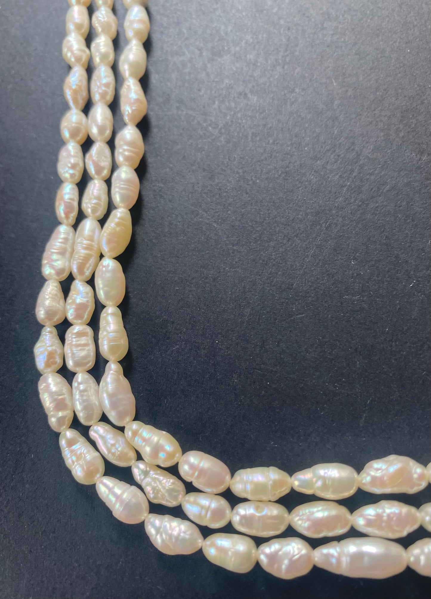 Strands of lustrous 5-5.5mm freshwater baroque rice pearl beads laid out on a dark black surface, highlighting their elegant.
