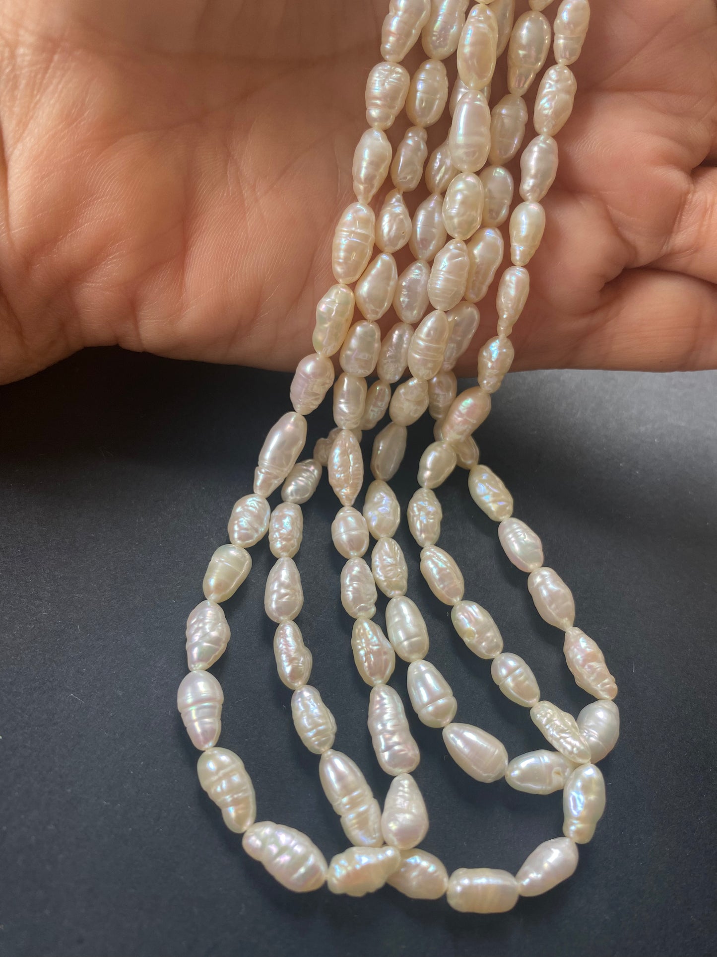 A hand delicately holds a strand of 5-5.5mm freshwater rice baroque pearls, showcasing their lustre and elegance.