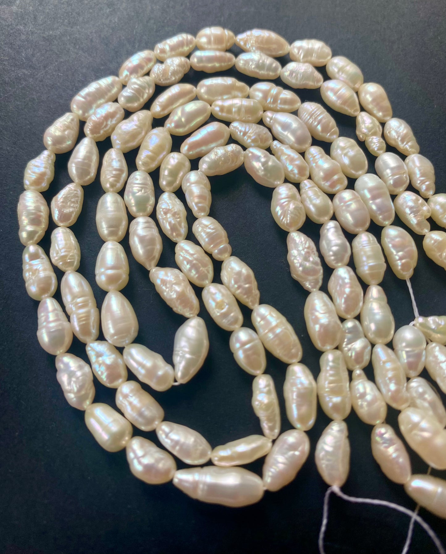 A strand of lustrous 5-5.5mm freshwater baroque rice pearl beads laid out on a dark black surface, highlighting their elegance.
