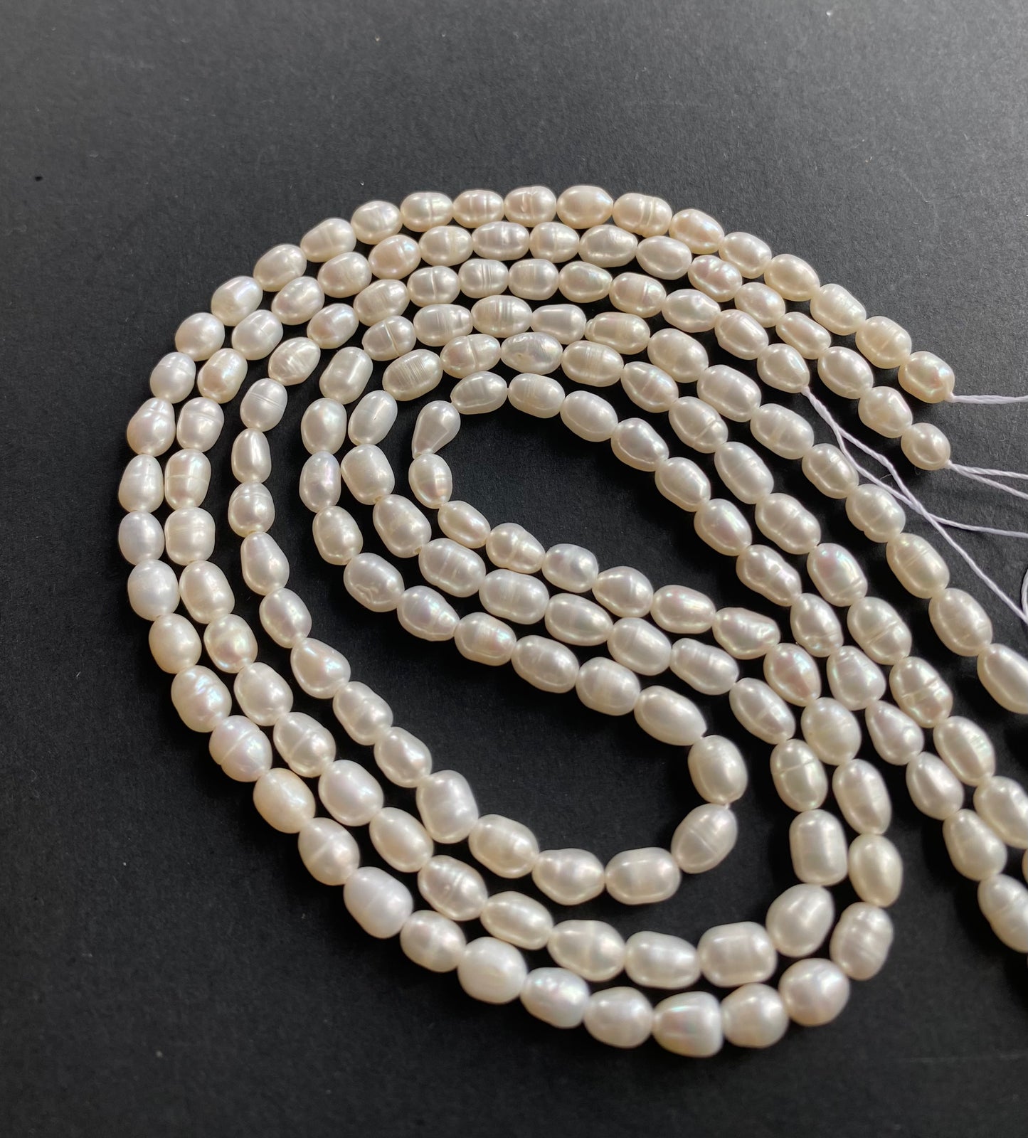 A delicate strand of 4-4.5mm freshwater pearl beads elegantly displayed on a smooth black surface.