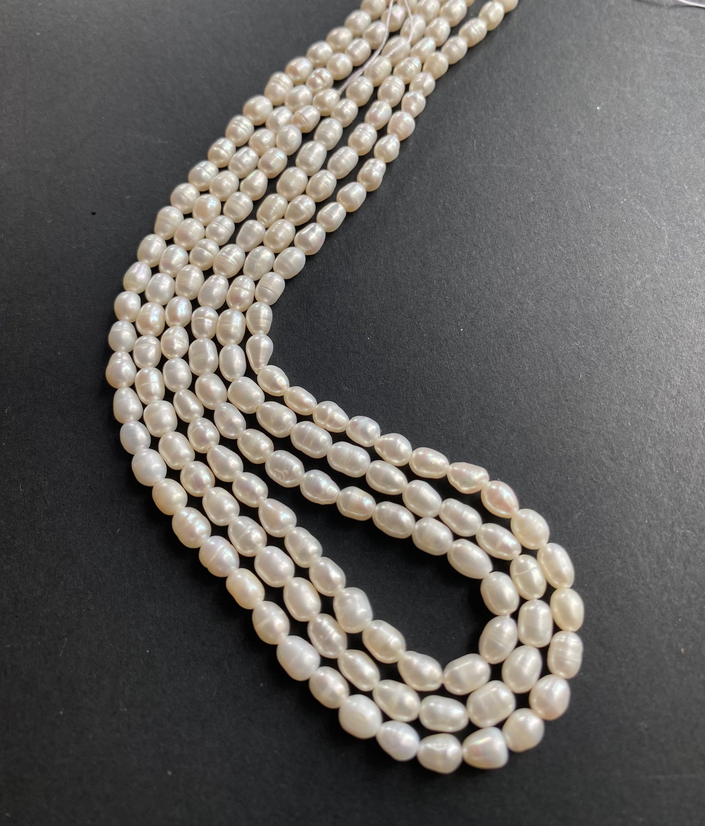 A strand of lustrous freshwater pearl beads laid out on a dark black surface, highlighting their elegance.