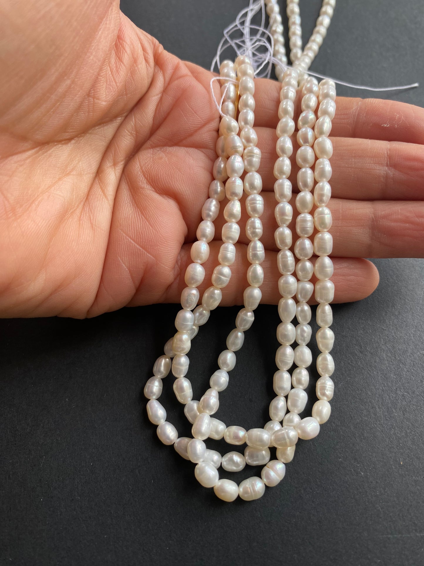 A hand delicately holds strands of 4-4.5mm freshwater pearl beads, showcasing their lustre and elegance.