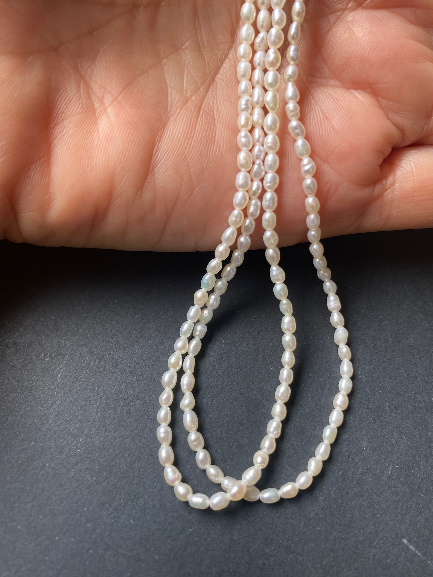 A hand delicately holds a strand of 2.5mm freshwater rice pearls, showcasing their lustre and elegance.