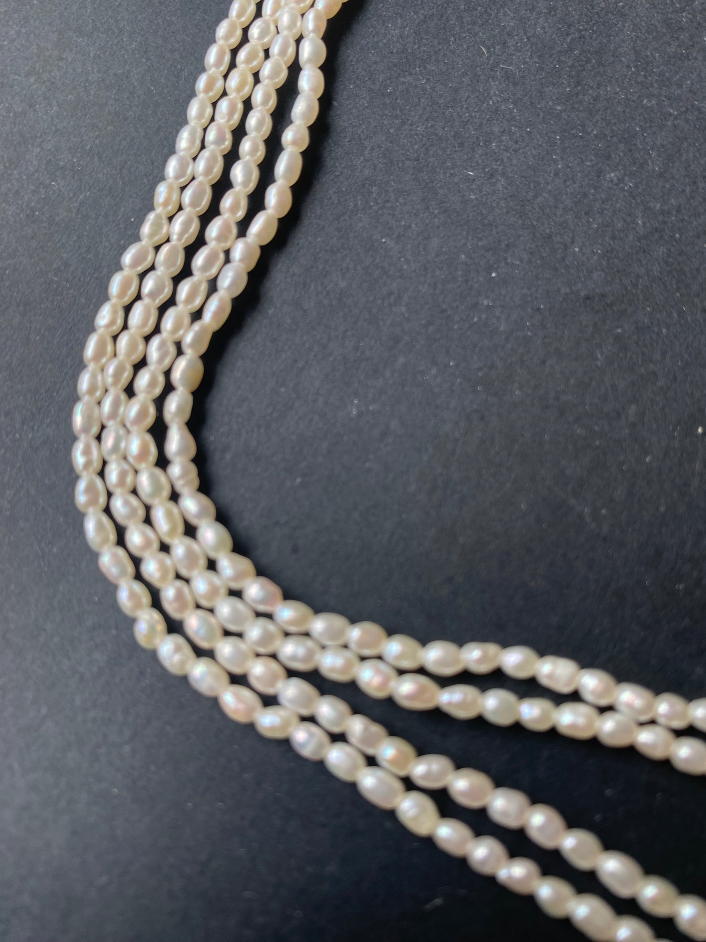 A beautiful strand of 2.5mm freshwater rice pearls resting on a sleek black background, showcasing their lustre.