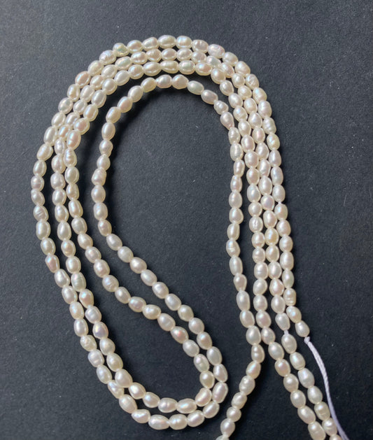 A strand of lustrous 2.5mm freshwater rice pearls laid out on a dark black surface, highlighting their elegance.