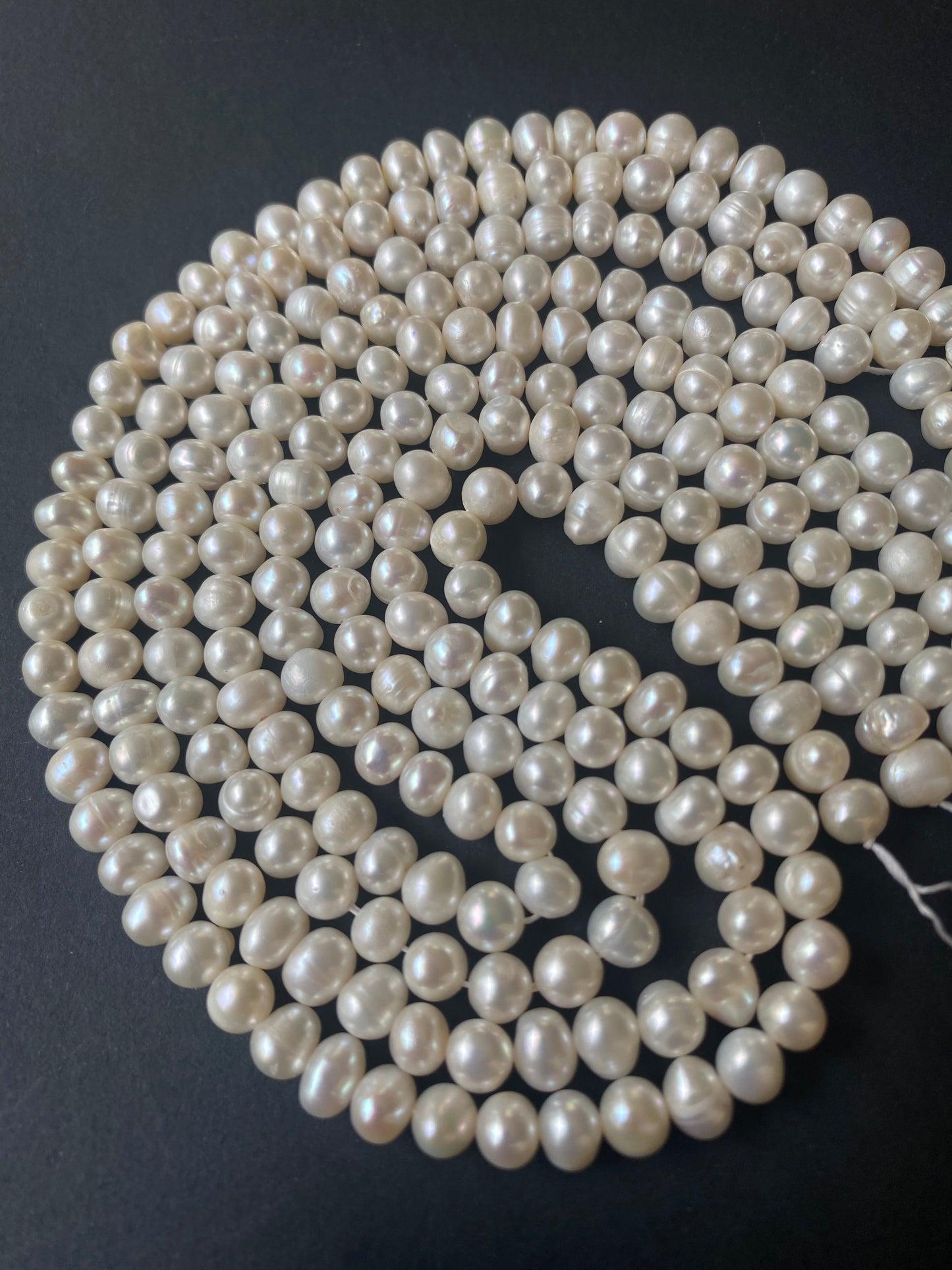 Strands of lustrous 6-6.5mm freshwater rice pearls laid out on a dark black surface, highlighting their elegance.