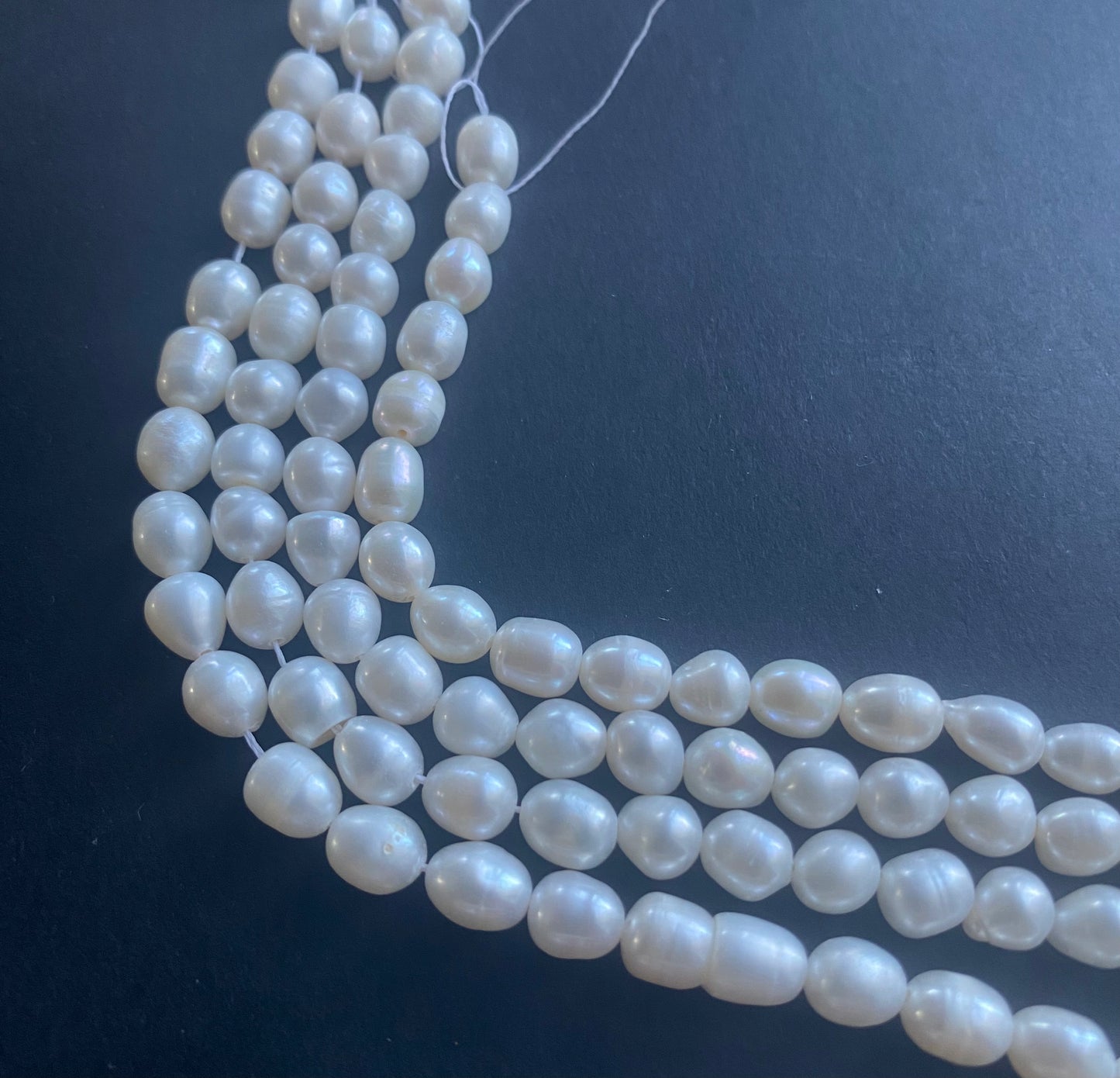 Delicate strands of 6mm freshwater pearl beads elegantly displayed on a smooth black surface.