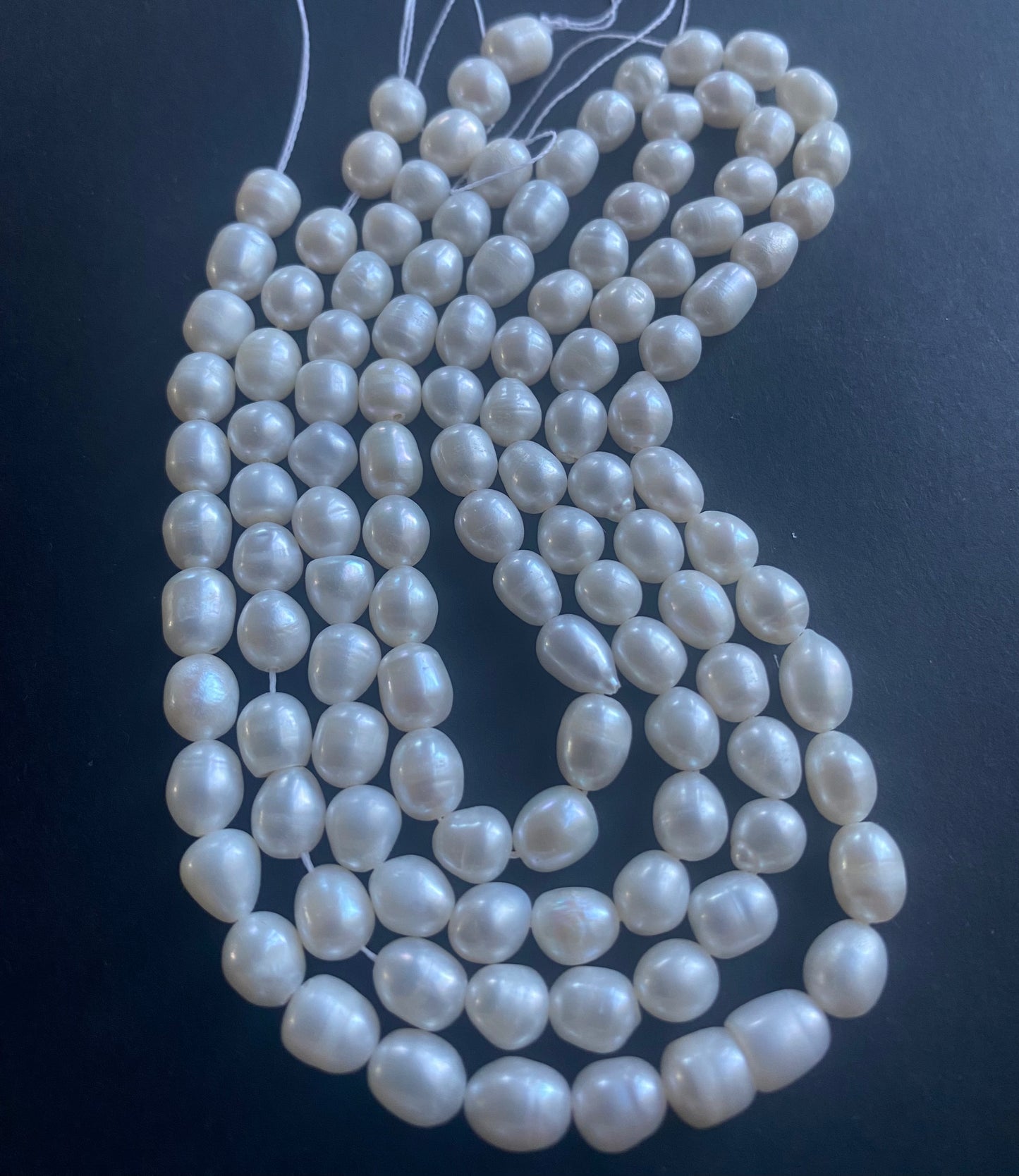 A strand of lustrous 6mm freshwater pearl beads laid out on a dark black surface, highlighting their elegance.