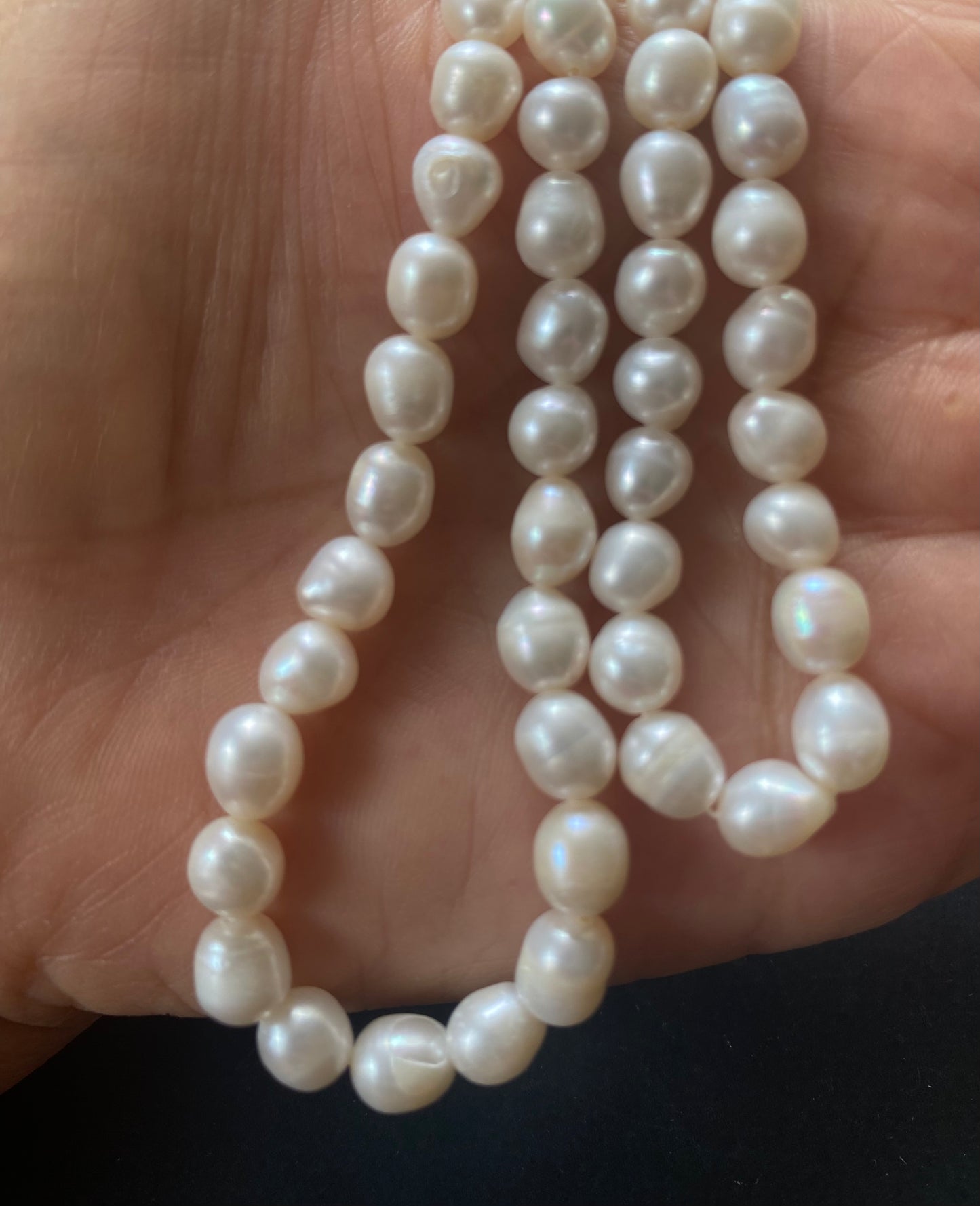 A hand delicately holds a strand of 6-6.3mm freshwater pearls, showcasing their lustre and elegance.