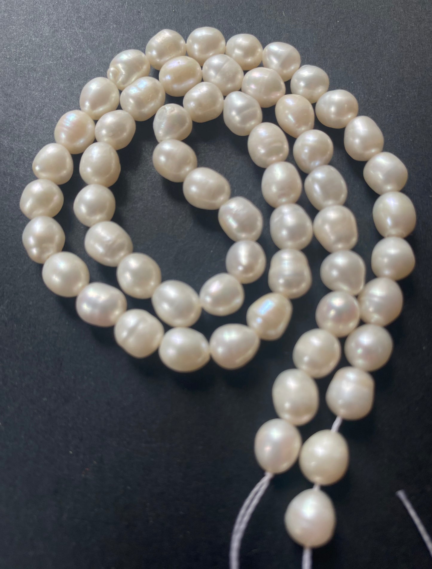 A strand of lustrous 6-6.3mm freshwater pearl beads laid out on a dark black surface, highlighting their elegance.