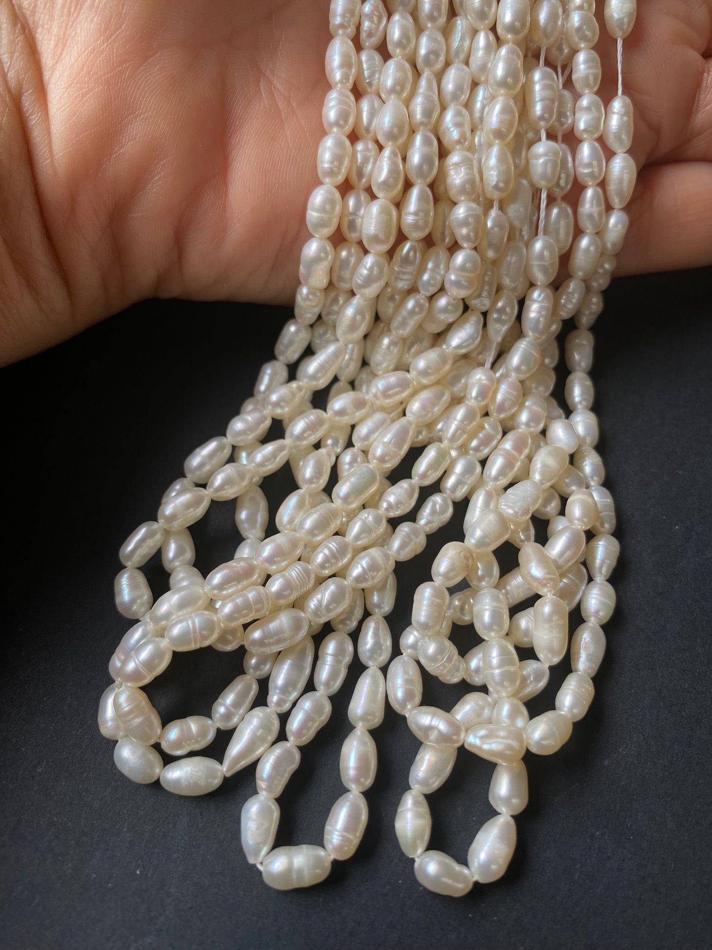 A hand delicately holds a strand of 4-4.5mm freshwater rice pearls, showcasing their lustre and elegance.