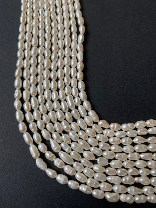 A beautiful strands of 4-4.5mm freshwater rice pearls resting on a sleek black background, showcasing their lustre.