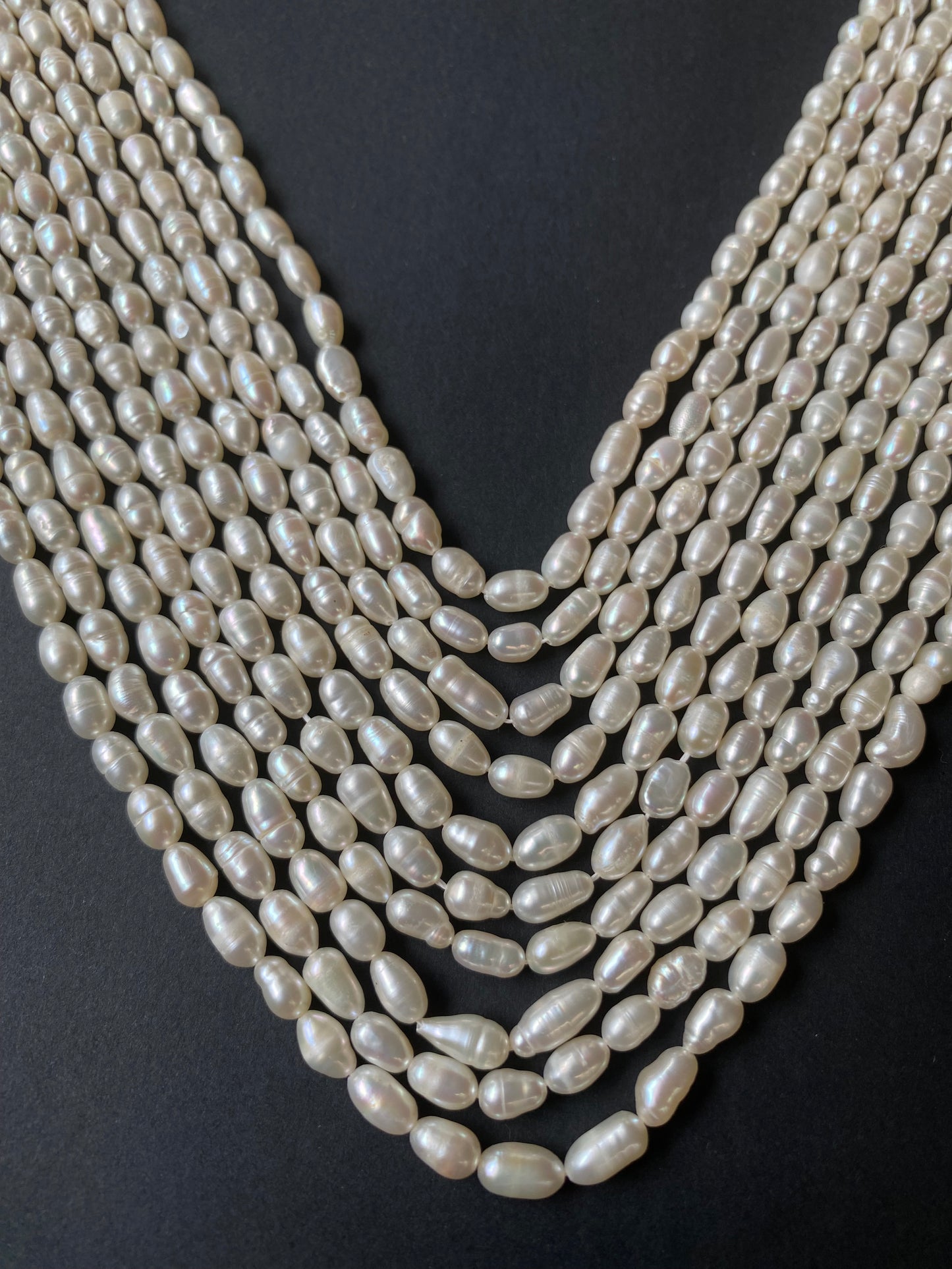 A delicate strands of 4-4.5mm freshwater rice pearls elegantly displayed on a smooth black surface.