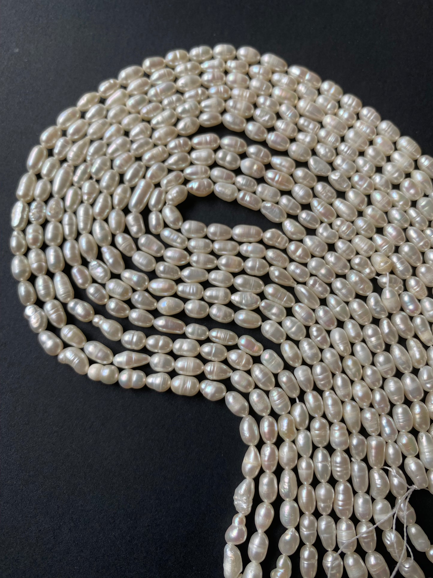 A strands of lustrous 4-4.5mm freshwater rice pearls laid out on a dark black surface, highlighting their elegance.