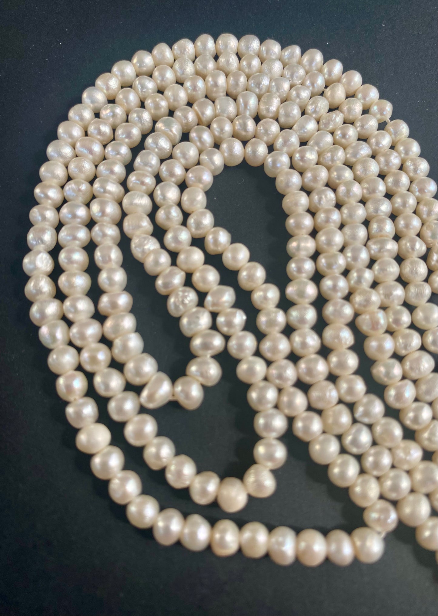 Strands of lustrous 5.5-6.0mm freshwater rice pearls laid out on a dark black surface, highlighting their elegance.