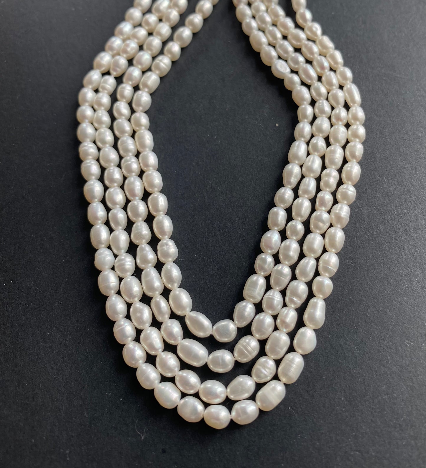 Beautiful strands of 4-4.5mm freshwater rice pearl beads resting on a sleek black background, showcasing their lustre.
