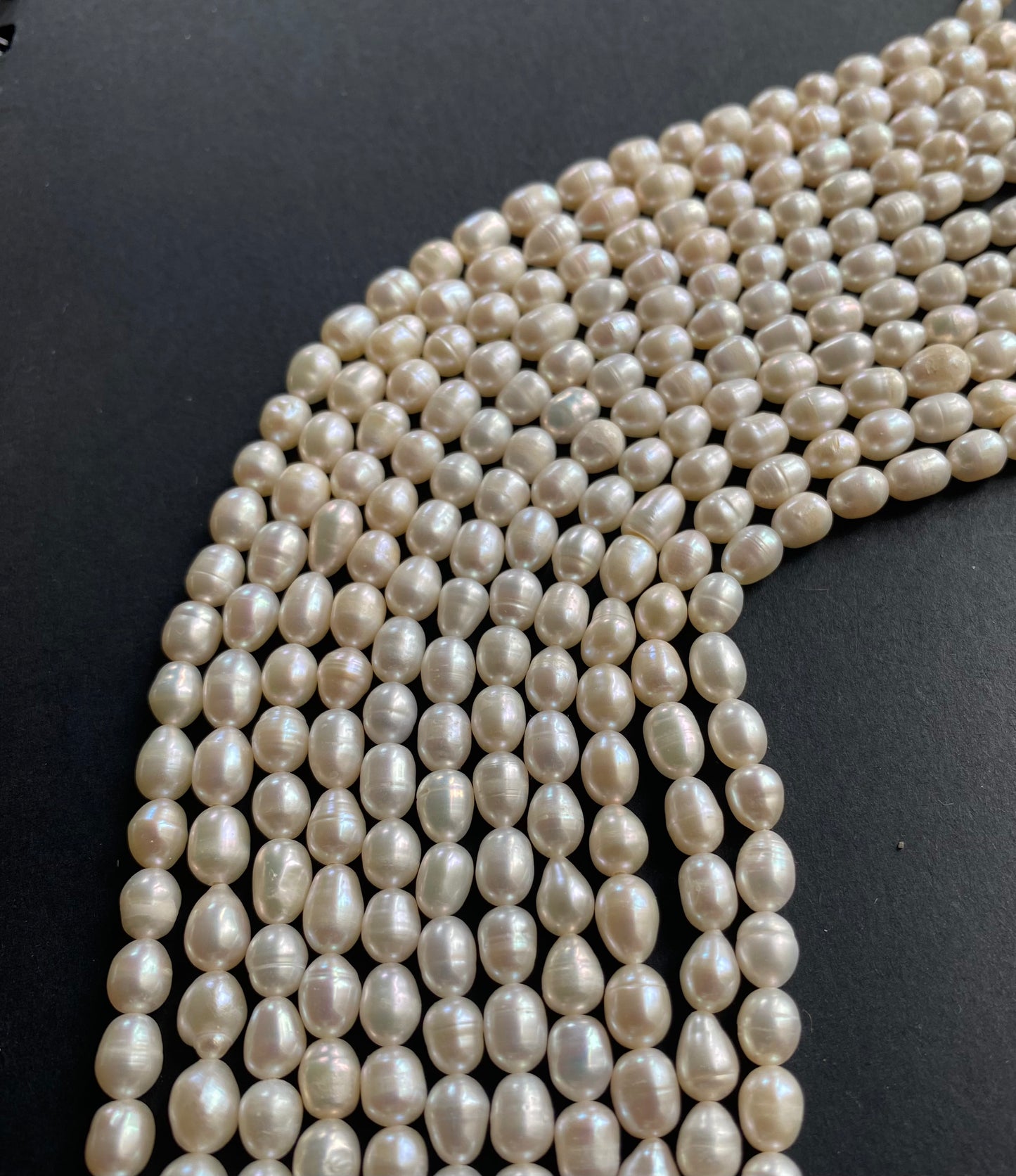 Delicate strands of freshwater rice pearl beads elegantly displayed on a smooth black surface.