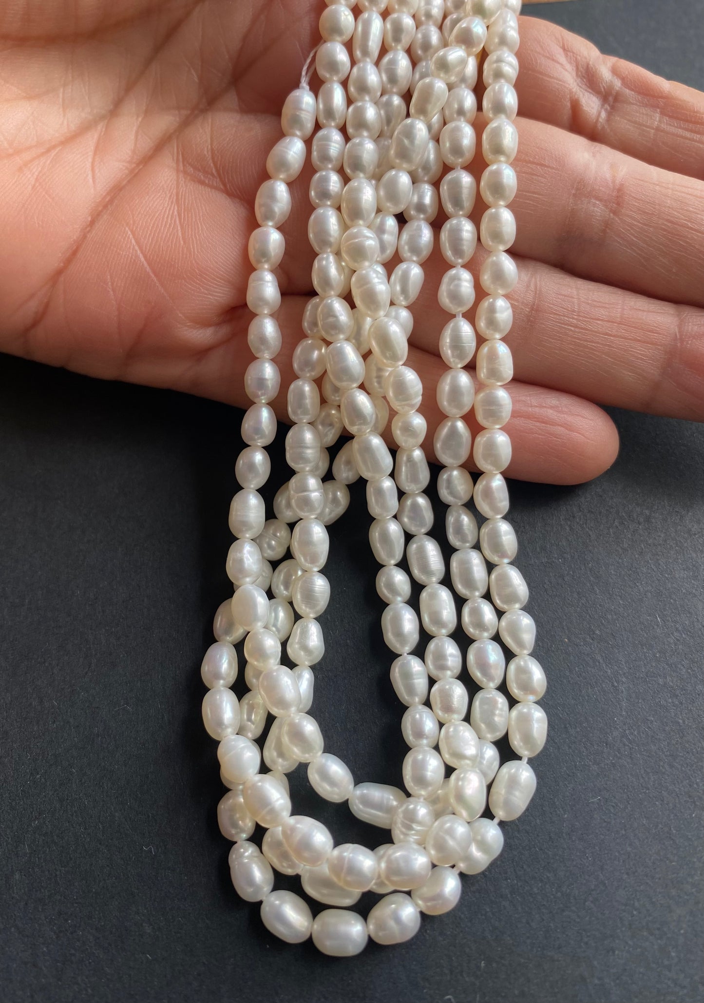 A hand delicately holds a strand of 4-4.5mm freshwater rice pearls, showcasing their lustre and elegance.