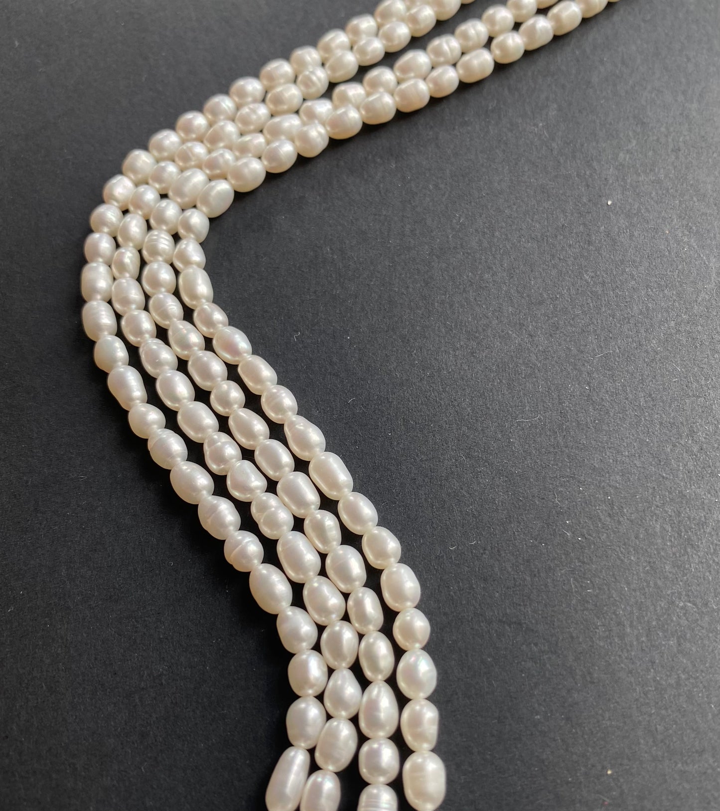 Delicate strands of 4-4.5mm freshwater rice pearl beads elegantly displayed on a smooth black surface.