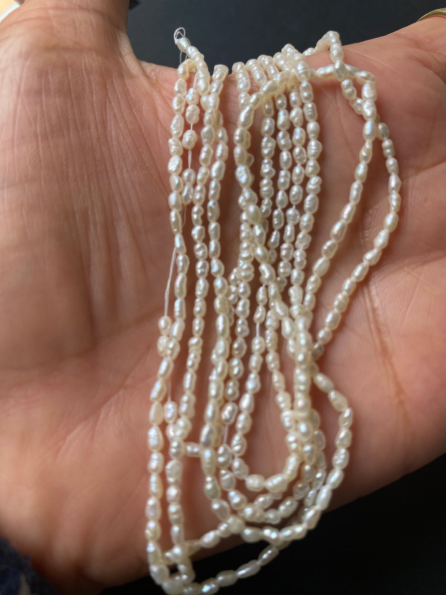 A person elegantly holds a delicate strand of freshwater rice pearls, measuring 2-2.2mm in size, showcasing their lustre.