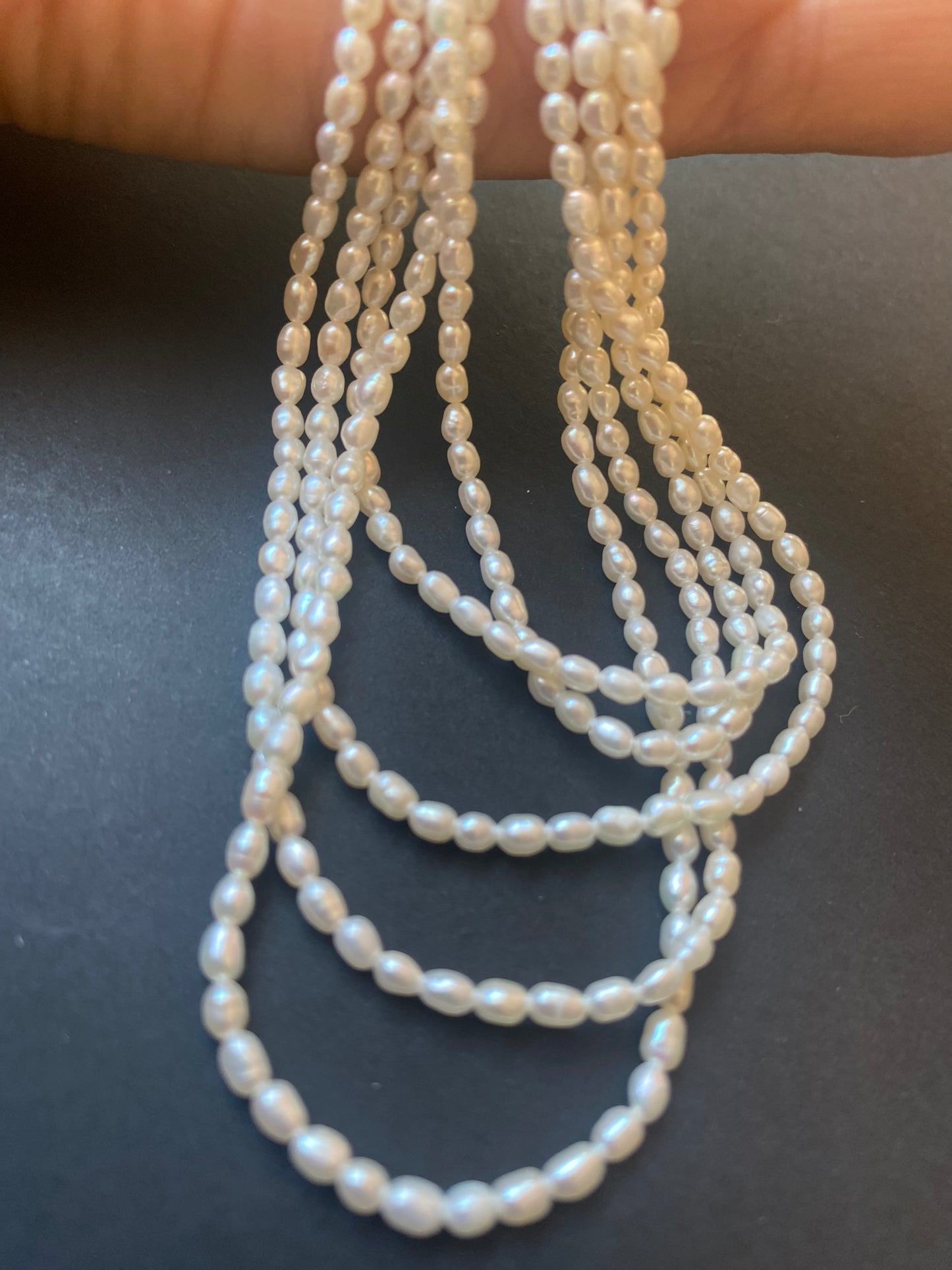 A close-up of a strands of 2.5-2.7mm freshwater rice pearls resting on a sleek black surface.