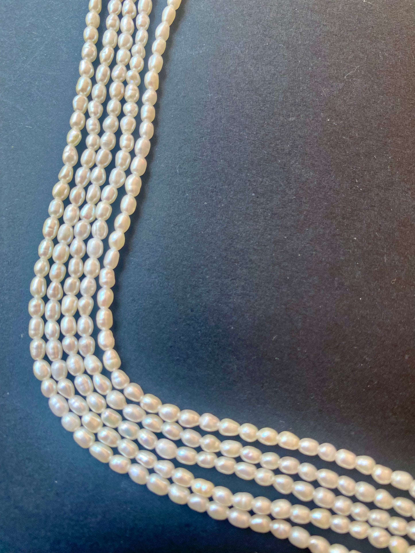 Delicate strands of 2.5-2.7mm freshwater rice pearls showcased against a dark black background.