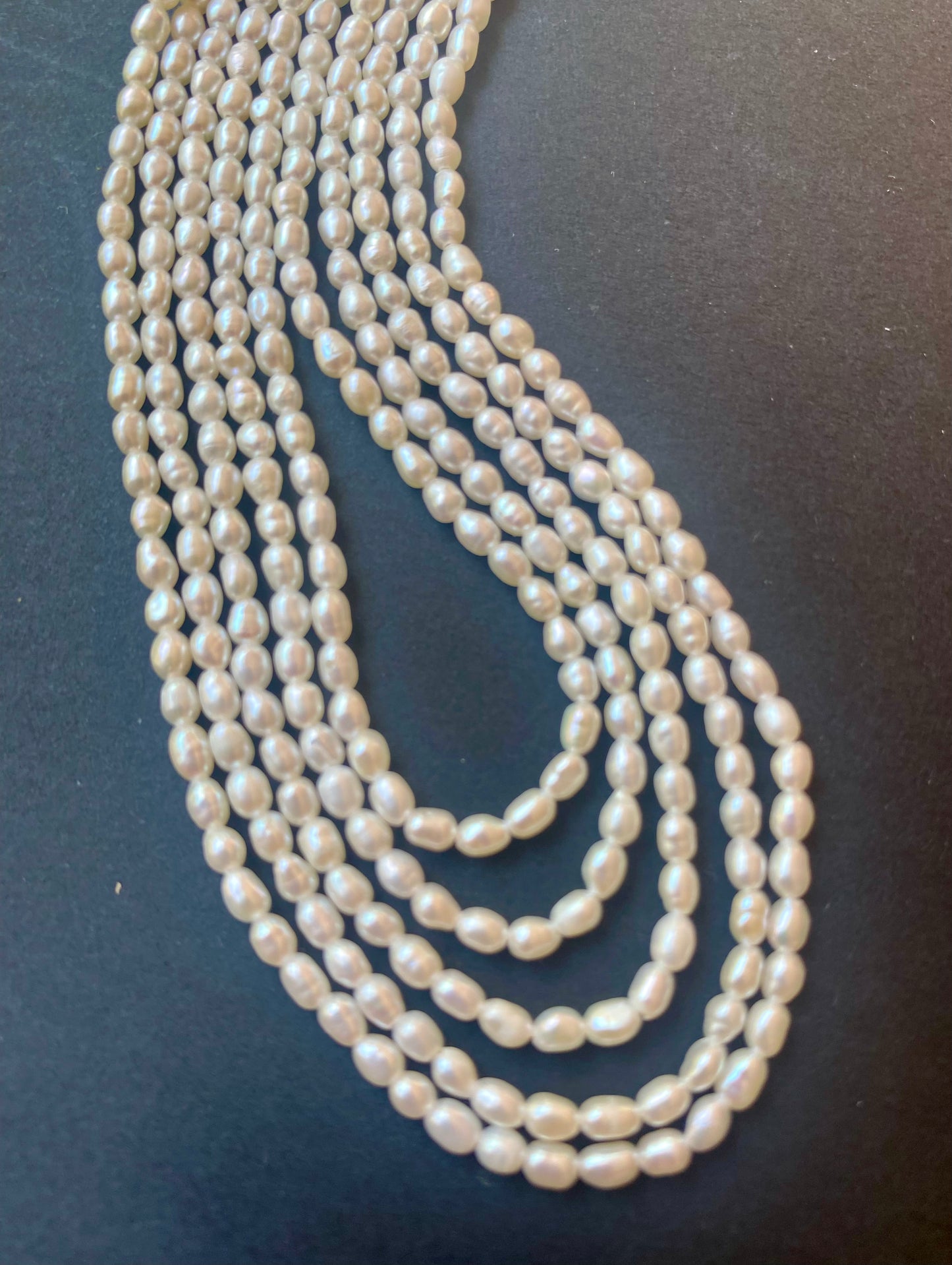 A strands of freshwater rice pearls, measuring 2.5-2.7mm, elegantly displayed on a black surface.