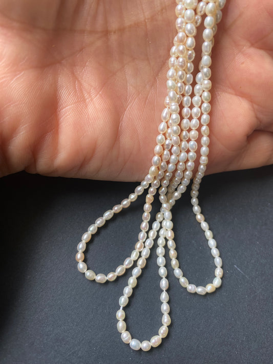A hand delicately holds a strand of 2.7mm freshwater rice pearls, showcasing their lustre and elegance.