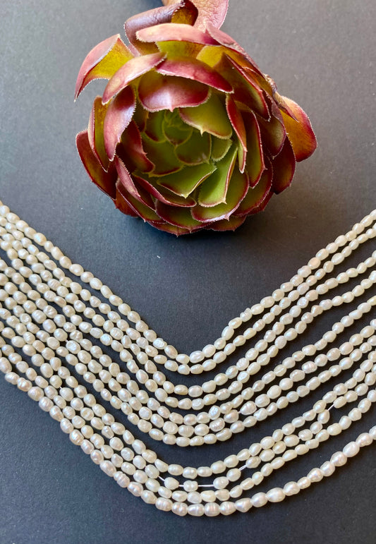 Strand of 2-2.5mm white freshwater rice pearls resting on a dark black surface, highlighting their lustre.