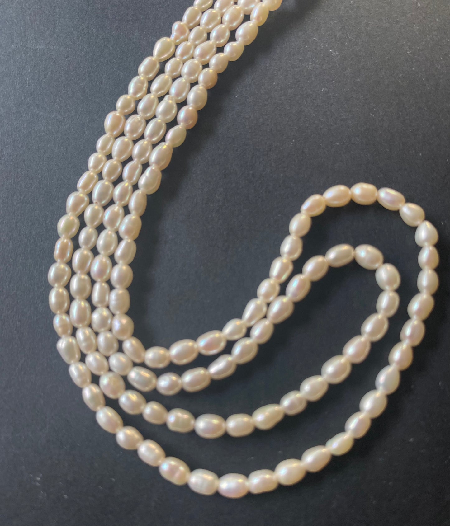A delicate strands of 3.0-3.2mm freshwater rice pearls elegantly displayed on a smooth black surface.